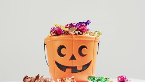 Scary-halloween-pumpkin-printed-bucket-full-of-candies-against-grey-background