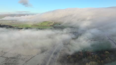 volando por encima de nubes bajas a la deriva y niebla con niebla que se mueve por la ladera de fondo cerca de la autopista m6 al amanecer en invierno