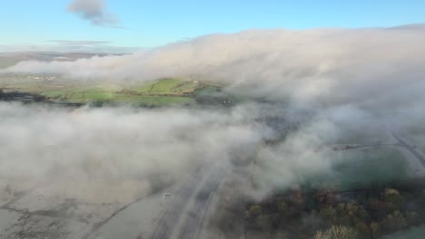 flying above low drifting cloud and mist with fog moving down background hillside near m6 motorway at dawn in winter