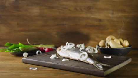 pouring onion rings onto marinated herring on wooden board