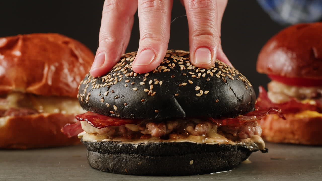 Close-up of a chef preparing a gourmet burger with a black bun.