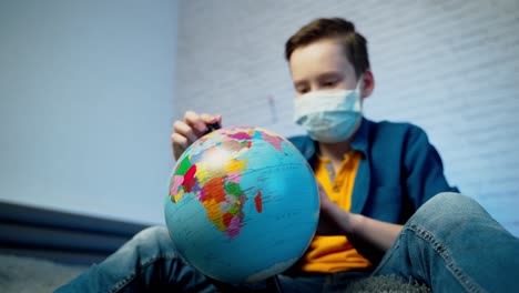 boy looking at globe learning about virus spreading around the world. boy wearing medical face mask. concept of covid-19 pandemic infection.