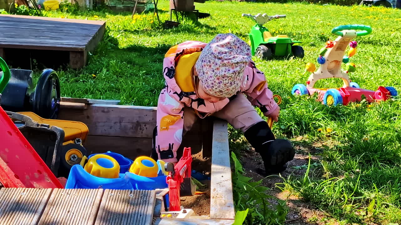 Toddler plays at sandbox surrounded by colorful ride-on toys in sunny backyard