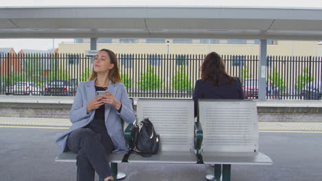 two businesswomen commuting to work waiting for train on station platform looking at mobile phones