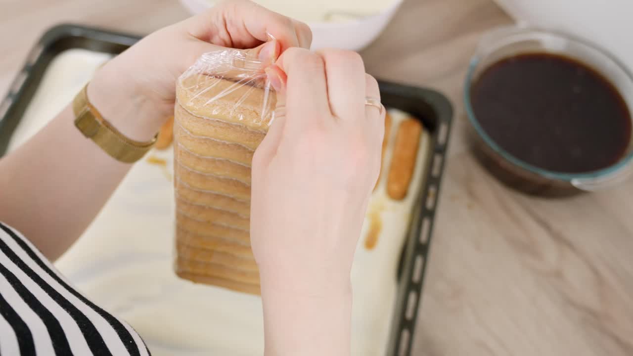 Woman opens package of ladyfingers to soak in dish for traditional tiramisu dessert preparation