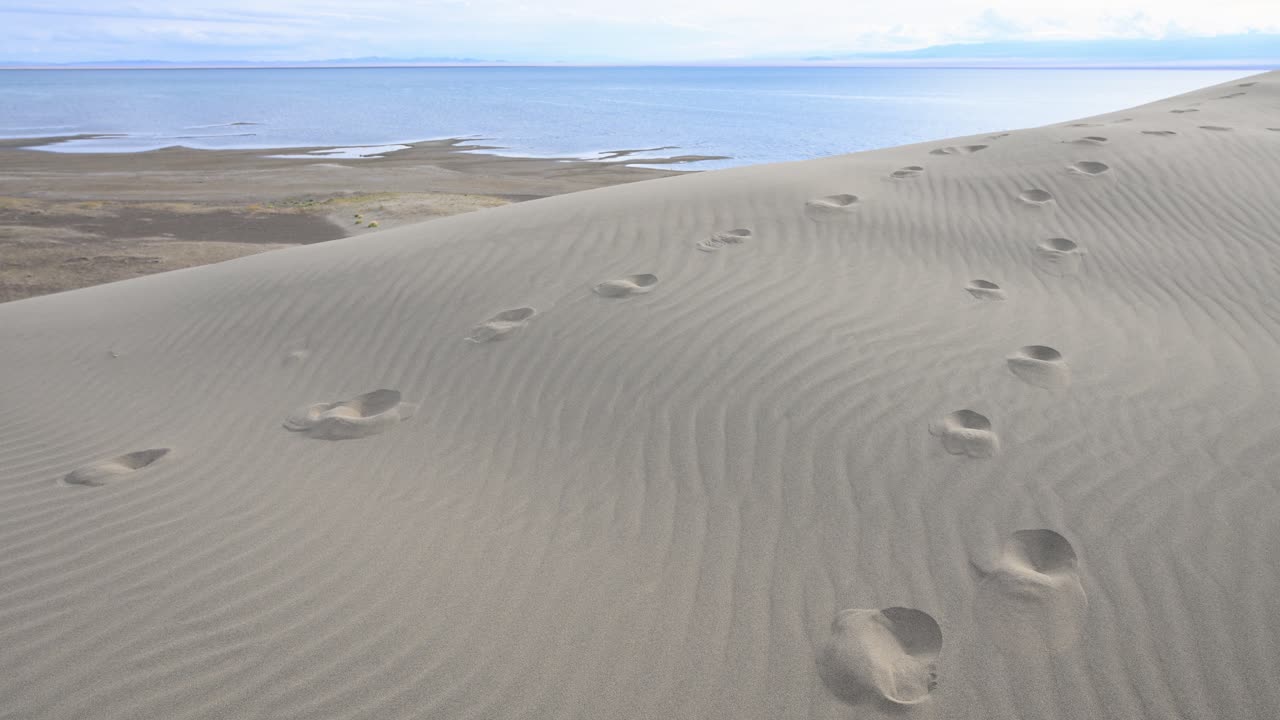 Two separate trails of footprints mark different paths across a sand dune beside Durgun Nuur lake, a metaphor for choices or diverging journeys