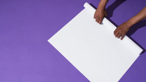 video of hands of african american man with rolling up white paper on purple background