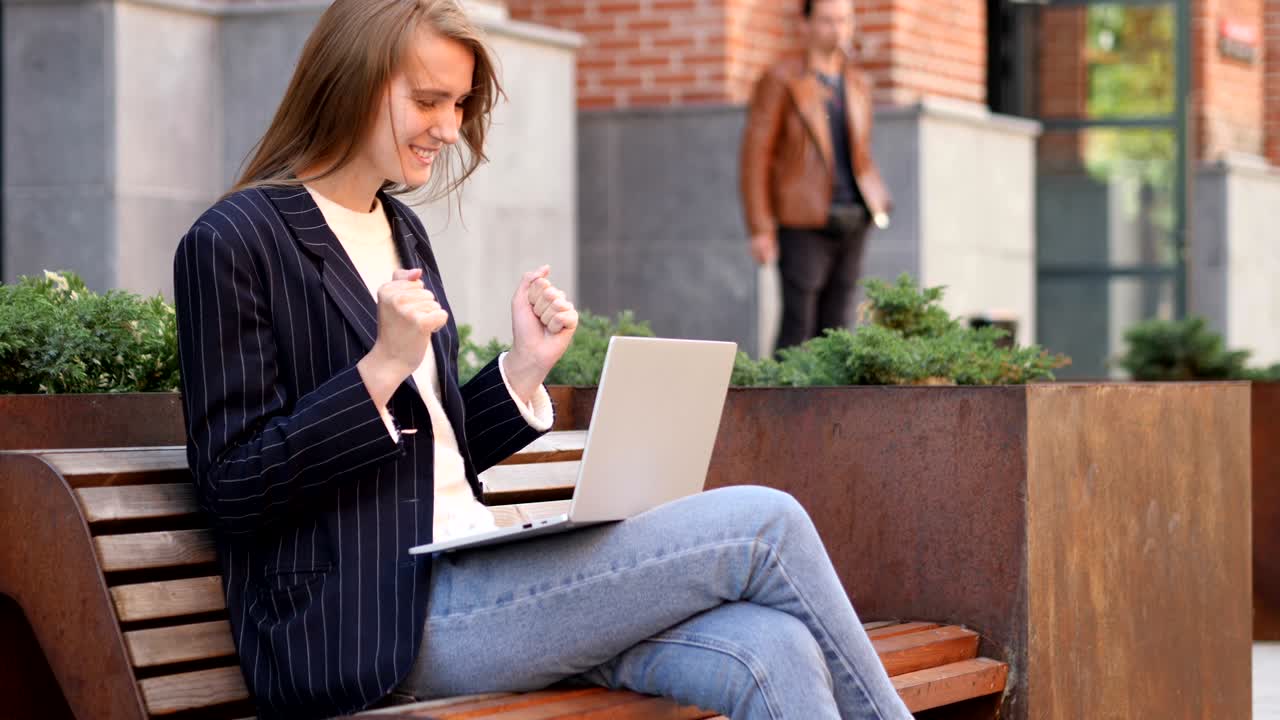 Excited Woman Celebrating Success on Laptop Sitting on Bench
