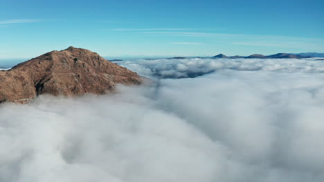 Mountain-peak-rising-above-sea-of-clouds-under-blue-sky,-majestic-natural-scenery