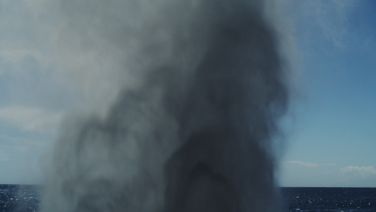 Midday ocean blowhole sends tall white spray into the sky in slow motion burst upward