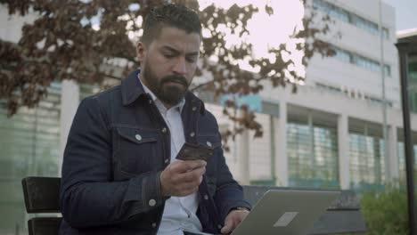 Man-holding-credit-card-and-using-laptop-outdoor