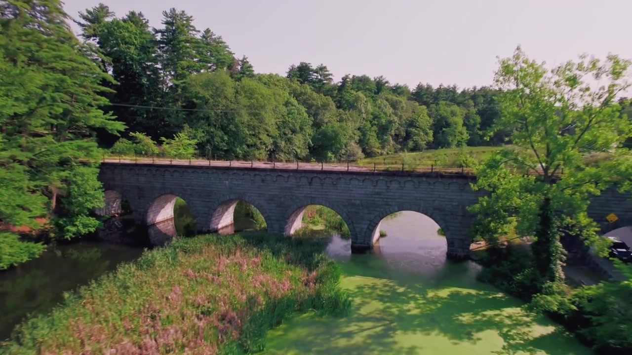 Drohne fliegt zurück und enthüllt eine weite Ansicht einer alten Steinbogen-Eisenbahnbrücke am Assabet River Stausee in Northborough, Massachusetts.