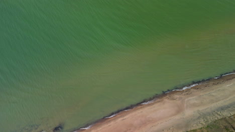 aerial top down view over coastal green waters with beach and grassy embankment with a drone tilt down shot