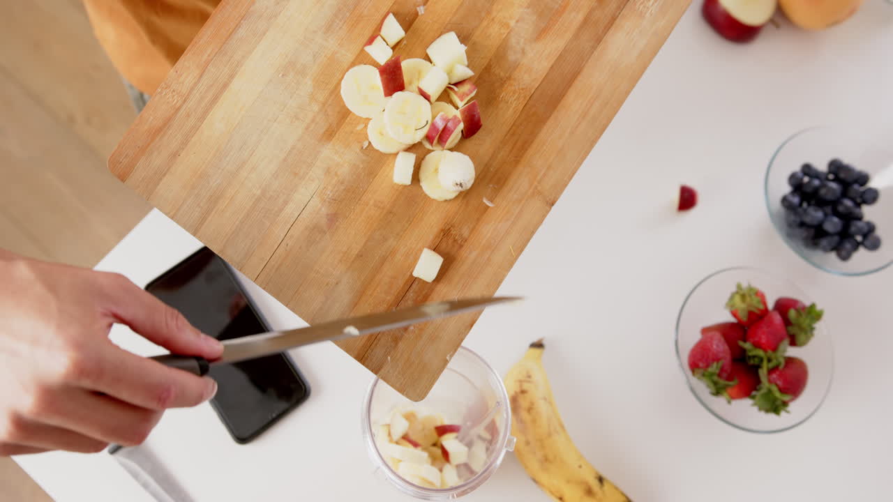 manos de un hombre biracial preparando un batido con frutas picadas en la cocina, espacio de copia, cámara lenta