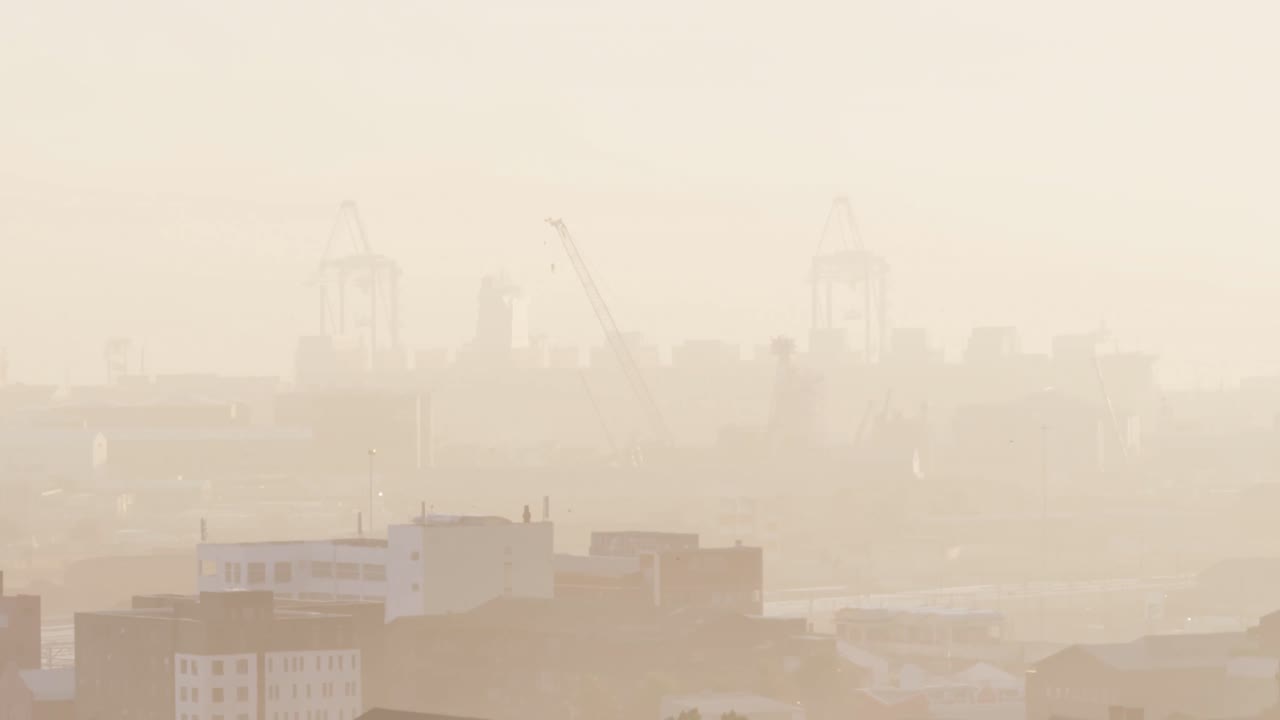 General view of cityscape with multiple buildings and shipyard covered in fog