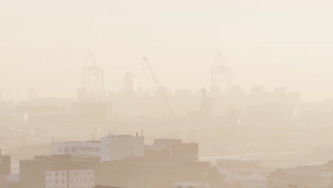 general view of cityscape with multiple buildings and shipyard covered in fog