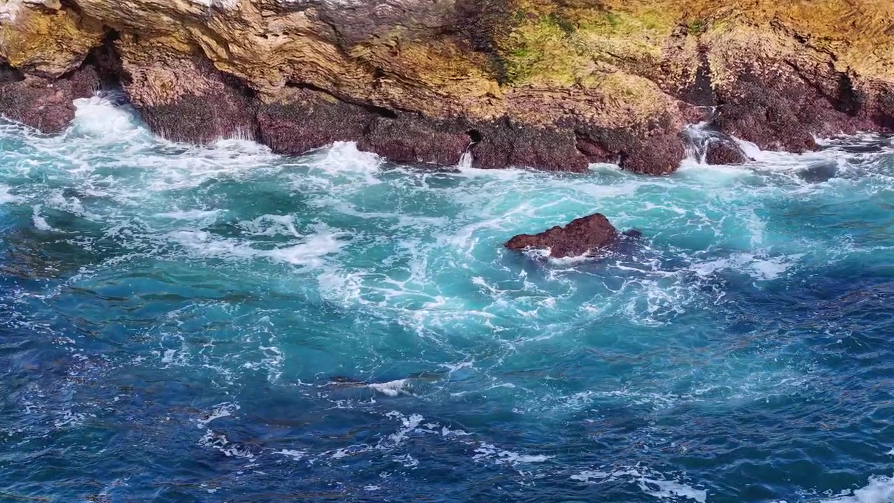 Litoral escarpado com águas azul-claras e ondas.