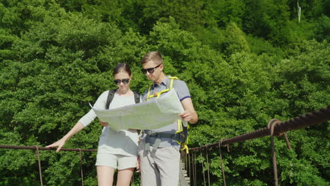 a man and a woman are studying the map they stand on the bridge in the background of a picturesque s