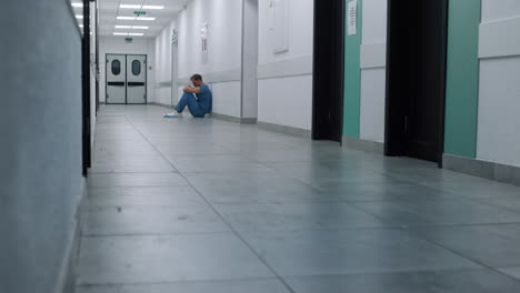 tired doctor sitting hospital corridor floor. overwhelmed surgeon resting alone.