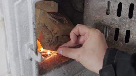 El-Hombre-Enciende-Un-Fósforo-E-Intenta-Encender-Leña-En-Una-Vieja-Estufa-De-Azulejos,-Luego-Cierra-La-Puerta