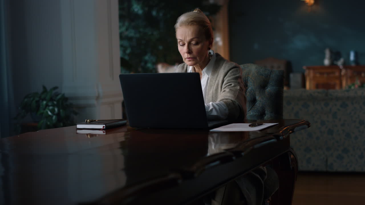 Rich mature woman typing laptop home. Greyhaired lady working computer cabinet.