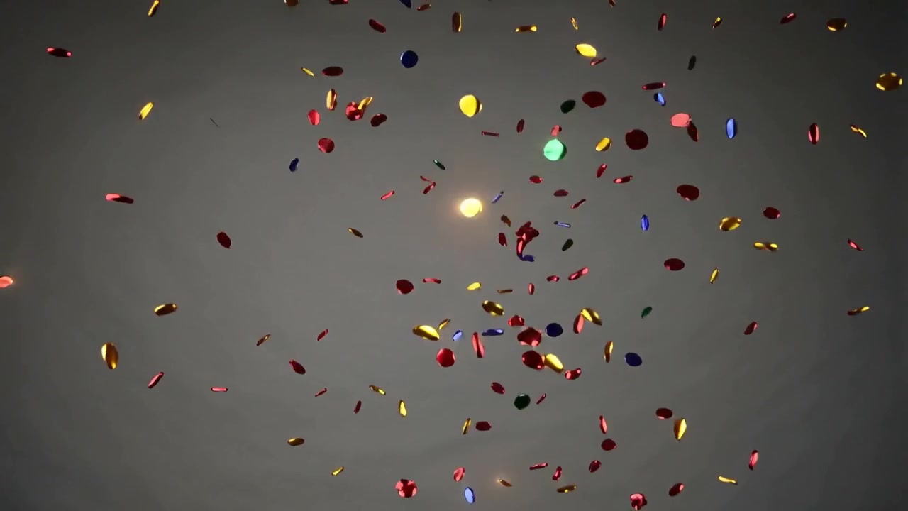 Coriandoli lucidi e colorati che cadono dall'alto, ruotando e spargendosi su uno sfondo grigio.