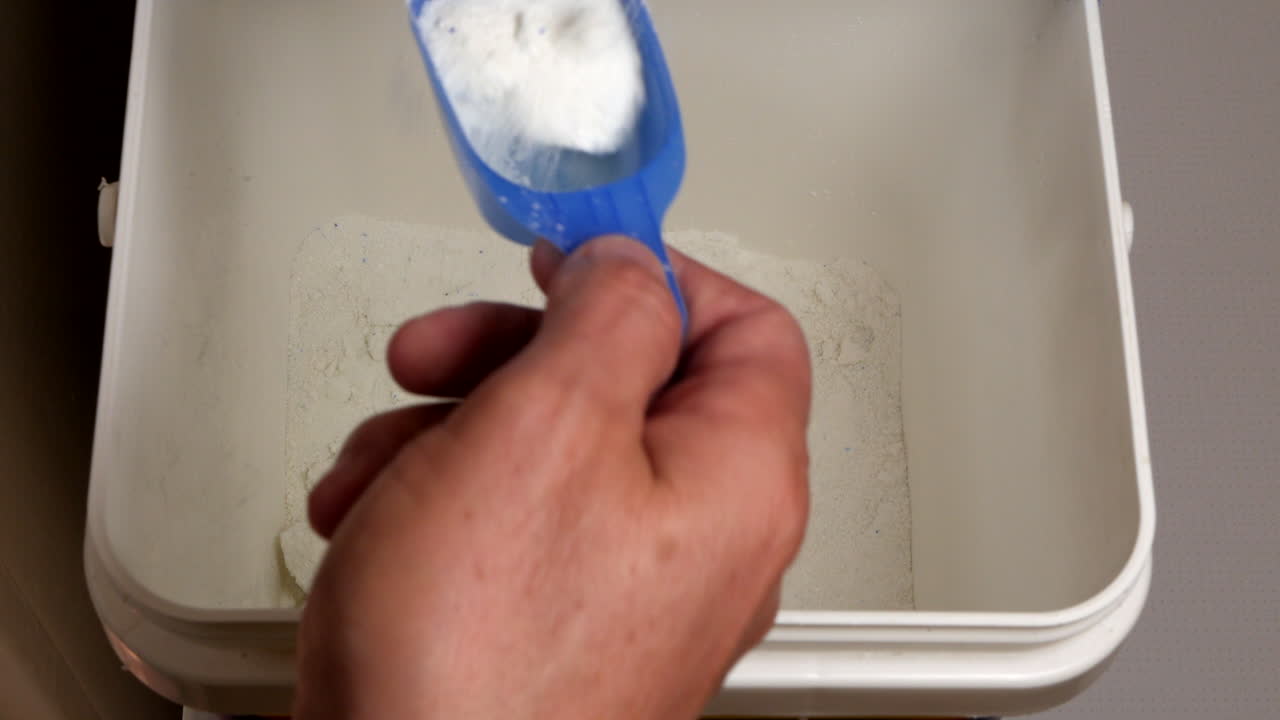 남자는 세탁기에 넣기 위해 측정 컵으로 세제를 퍼낸다