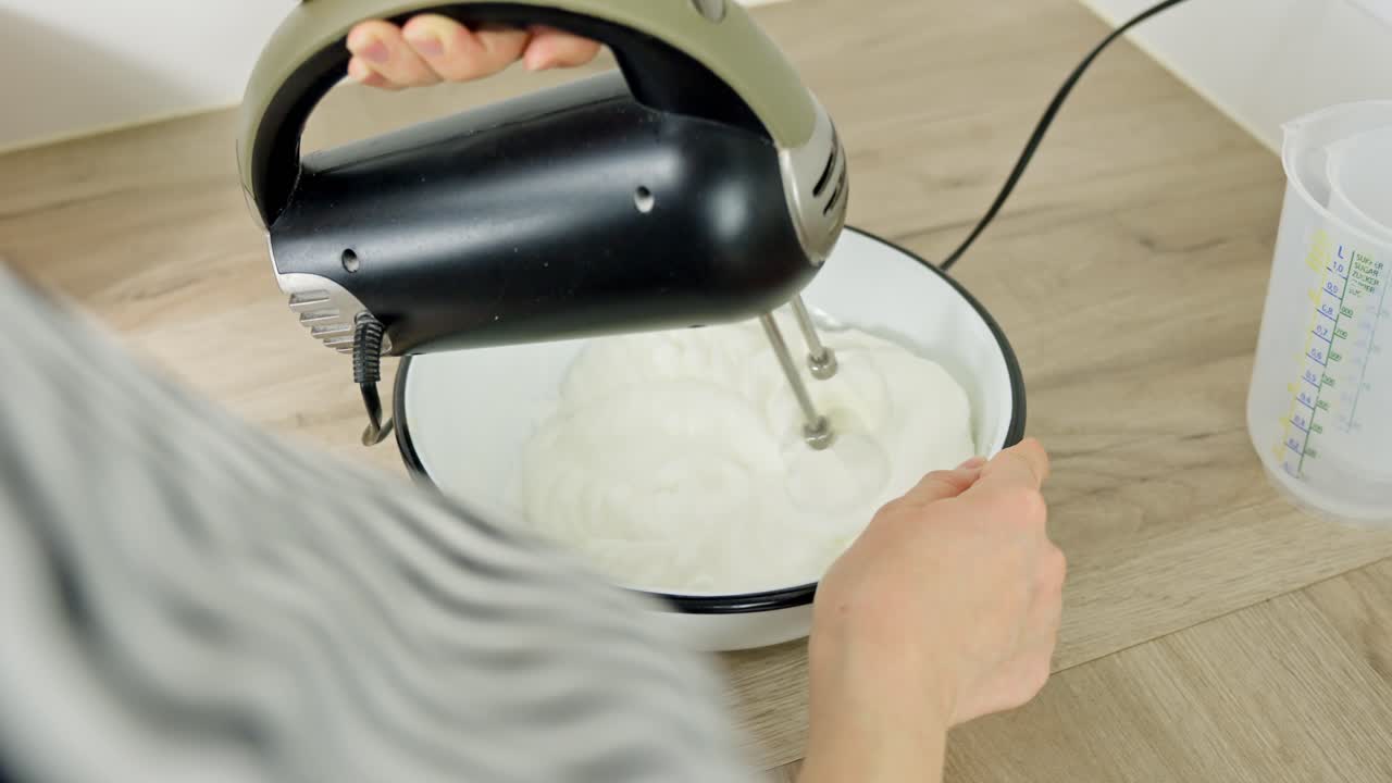 Mixing egg whites with a hand mixer in a bowl, preparing for a recipe