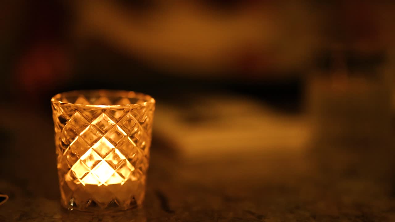 A candle flickers gently in a dimly lit, warm environment, creating a serene and intimate atmosphere