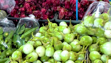 a colorful array of tropical produce including bitter melon, eggplants, mangoes, and bananas at a market stall.
