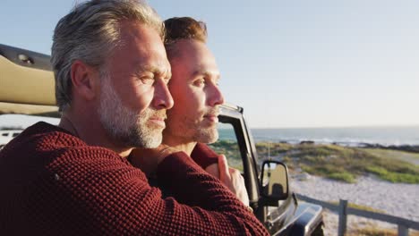 Happy-caucasian-gay-male-couple-standing-by-car-embracing,-admiring-view-on-sunny-day-at-the-beach