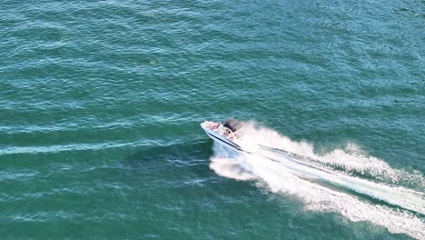 following a speed boat driving fast through the scene on an open blue lake in bright daylight aerial trucking follow