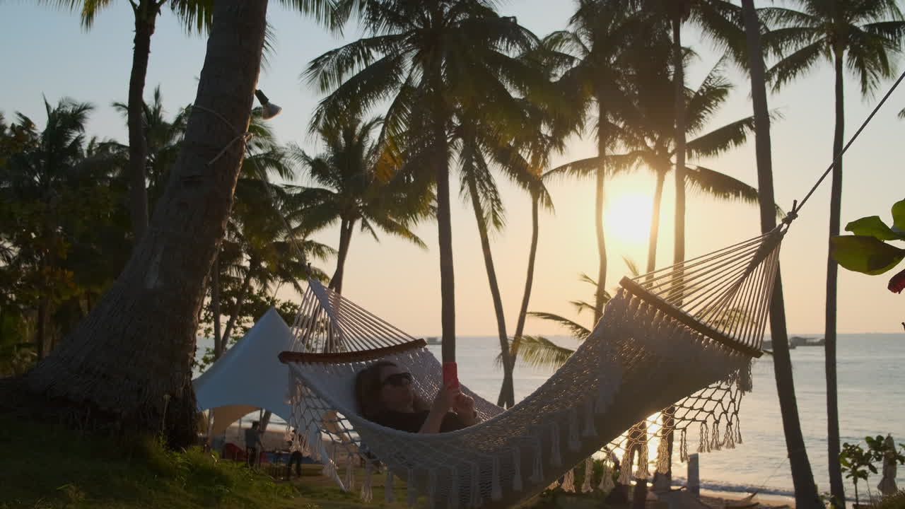mujer relajándose en una hamaca al atardecer en una playa tropical