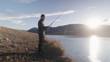 joven pescador arrastrando el señuelo de vuelta durante la puesta de sol sobre las montañas