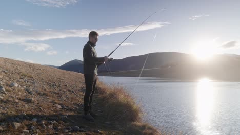 young fisherman reeling lure back in during sunset above mountains