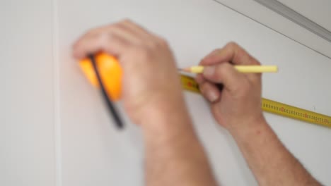 man measuring and marking a wall with a pencil and tape measure