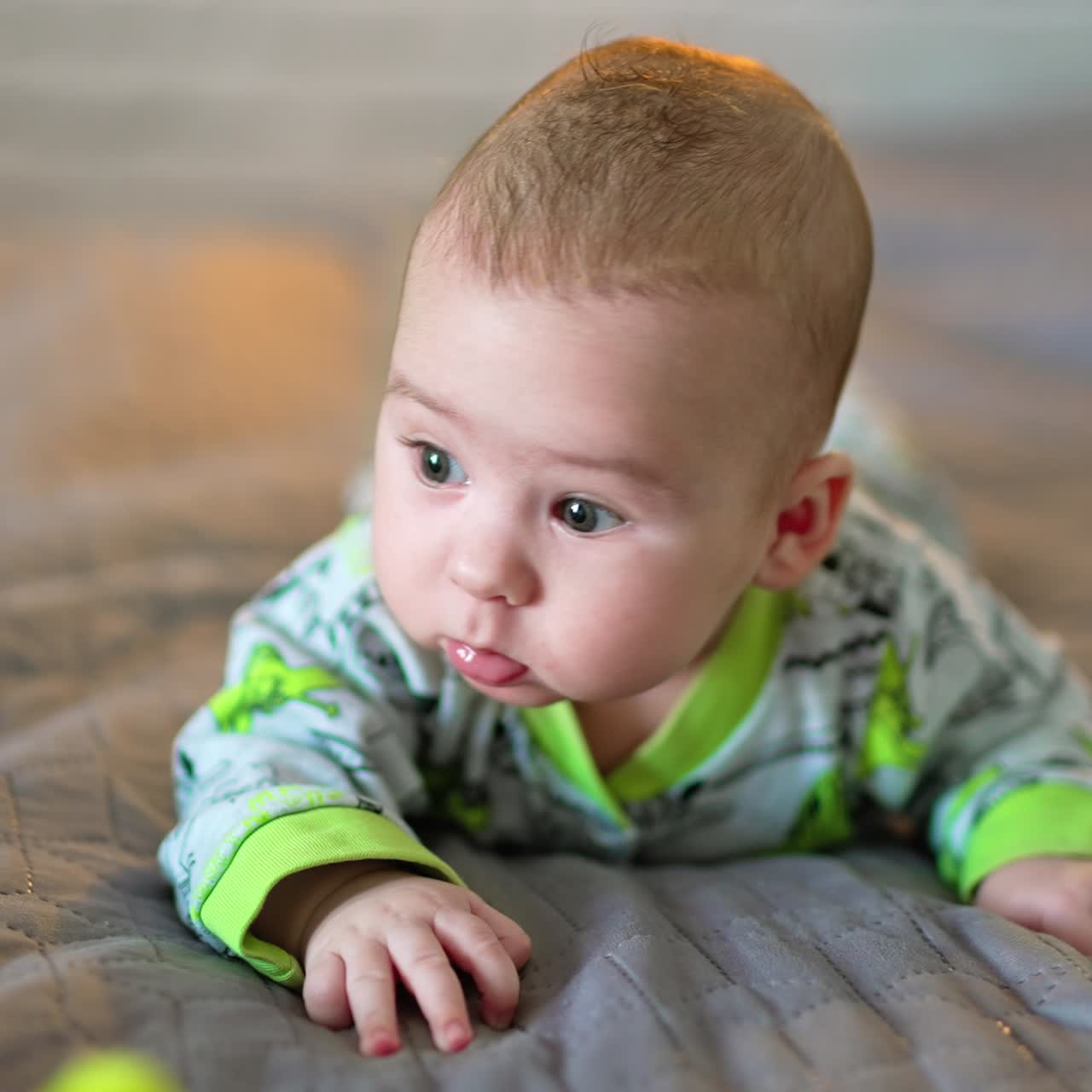 Sweet funny toddler lies on grey plaid and wants to get to the toy. Healthy Caucasian child on the blurred background