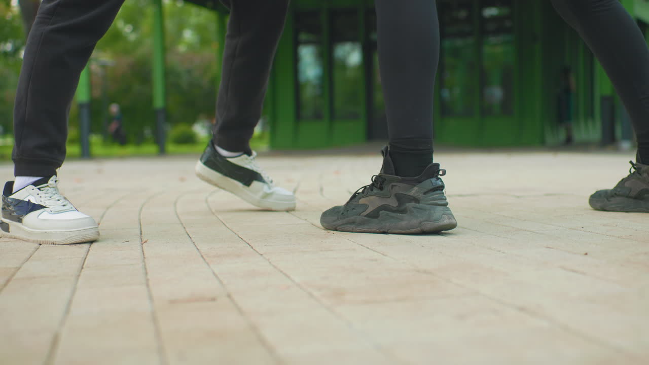 park pavement closeup two dancers feet duel, energetic youth practicing quick steps and rhythm on tiled plaza, casual white and black sneakers, close leg angles, focused footwork and playful