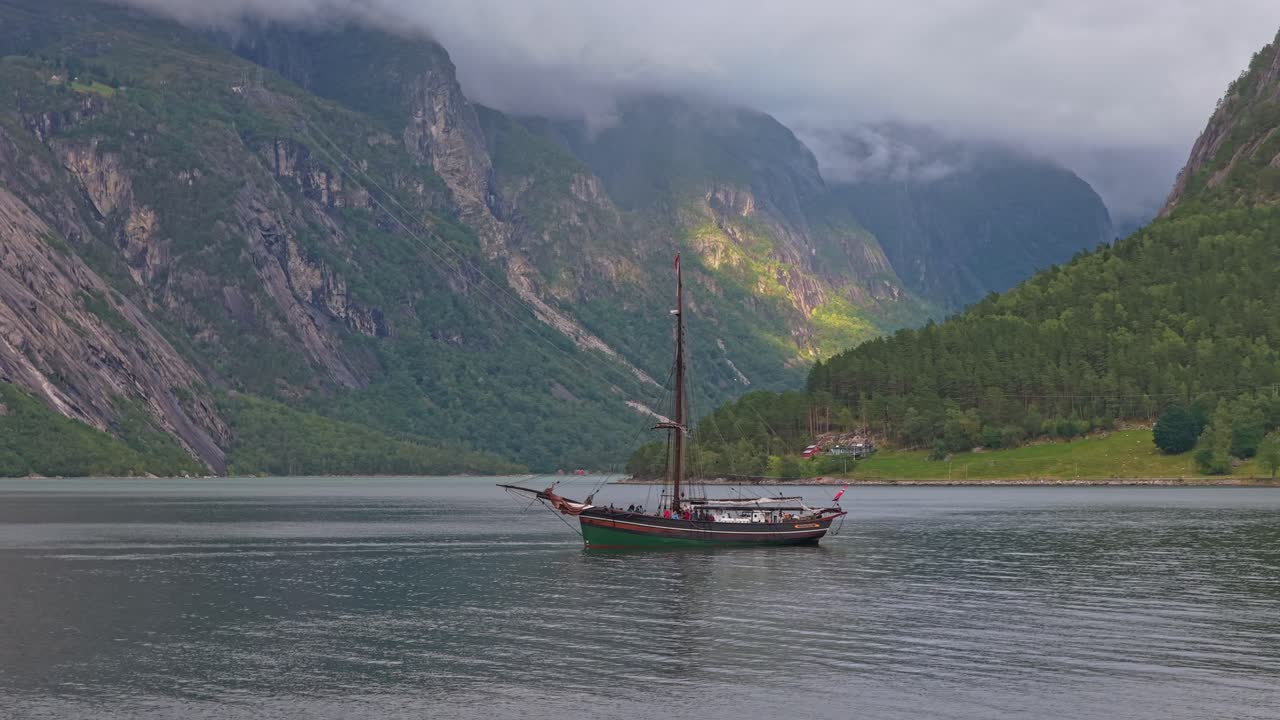 Film z lotu ptaka przedstawiający tradycyjny jacht żaglowy zacumowany w norweskim fiordzie.