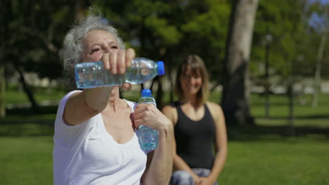 una mujer mayor sonriente entrenando con botellas de agua en el parque.