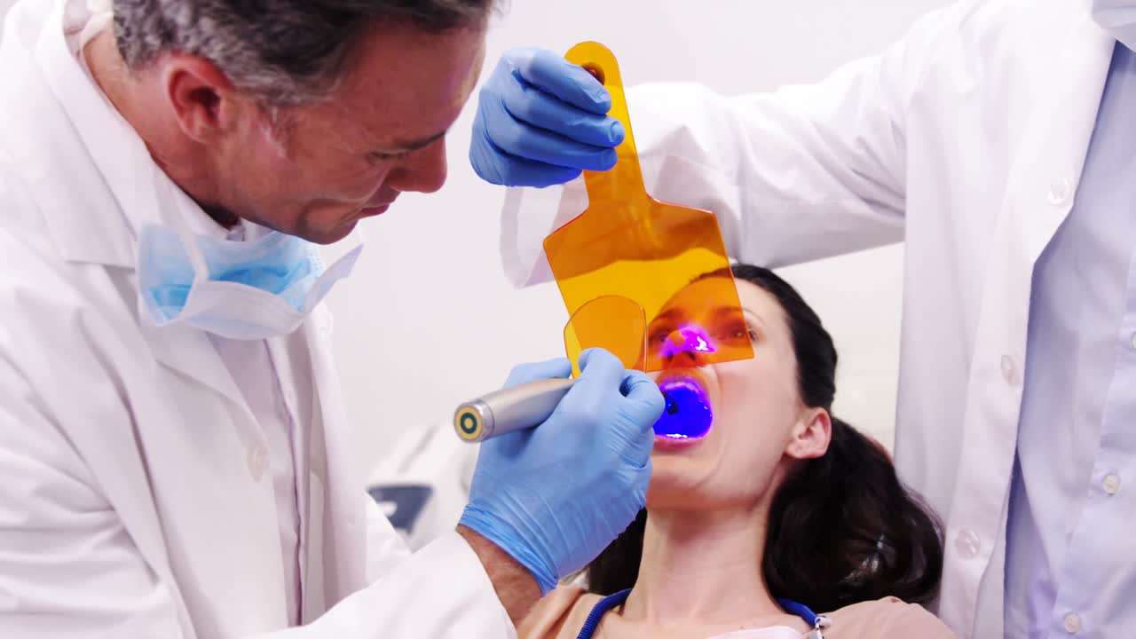 Dentisti esaminando paziente femminile con lampada fotopolimerizzante dentale