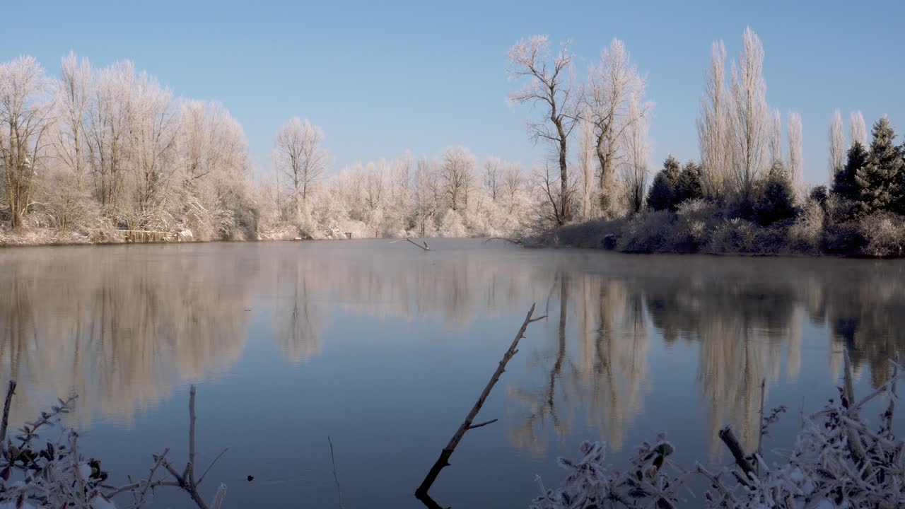 눈 덮인 나무들이 늘어선 잔잔한 강의 느린 추적 와이드 샷