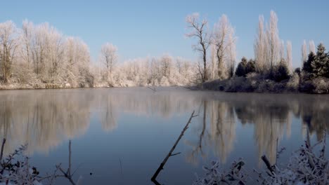 slow tracking wide shot of a calm river lined with snow-covered trees