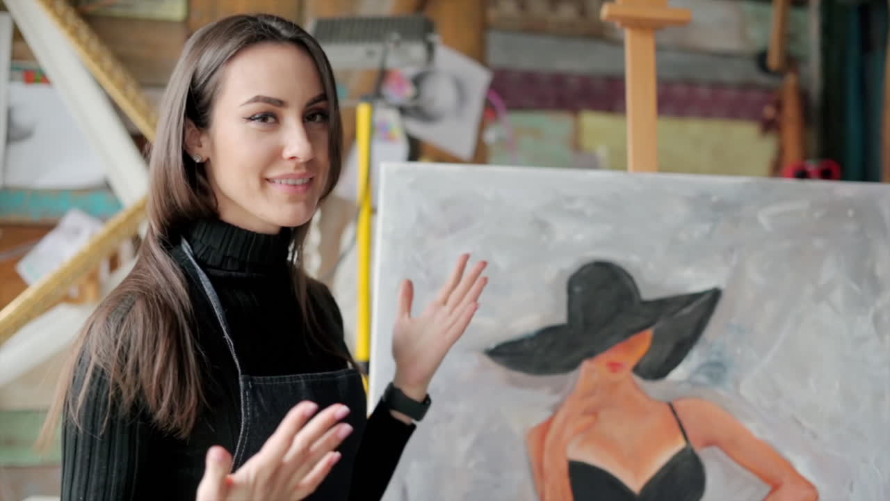 Woman painter wearing black clothes painting woman model face with hat drawing with red brush at a workshop