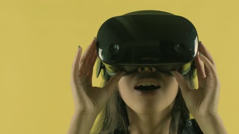 young woman looks around and wonders how amazing  in the vr world. virtual reality helmet on the yellow background. portrait