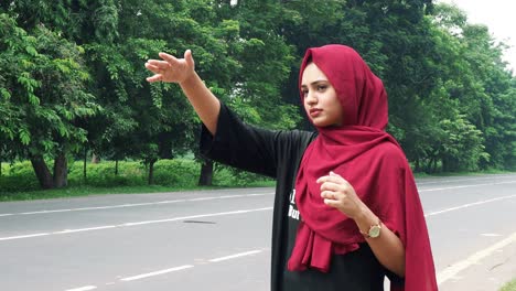 slow motion of a young smiling afghan girl in hijab in a black and red dress standing on the side of the road waiting for public transport to go back home