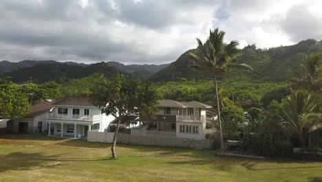 hd drone footage unveiling oahu’s north shore mountains behind charming local homes. showcasing a stunning contrast between lush green peaks and the island’s relaxed residential beauty.