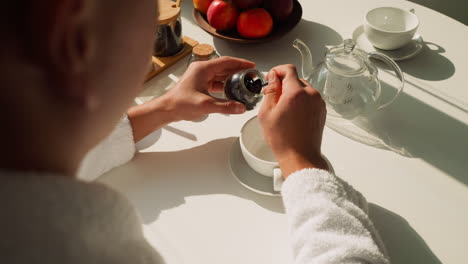 man scoops dried tea leaves into small spoon. young man aims savoring herbal infusion healthful attributes at table. potential health advantages