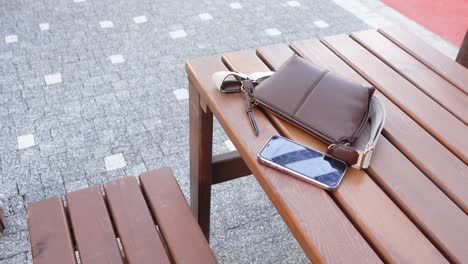 a brown leather purse and a black cellphone on a wooden table.