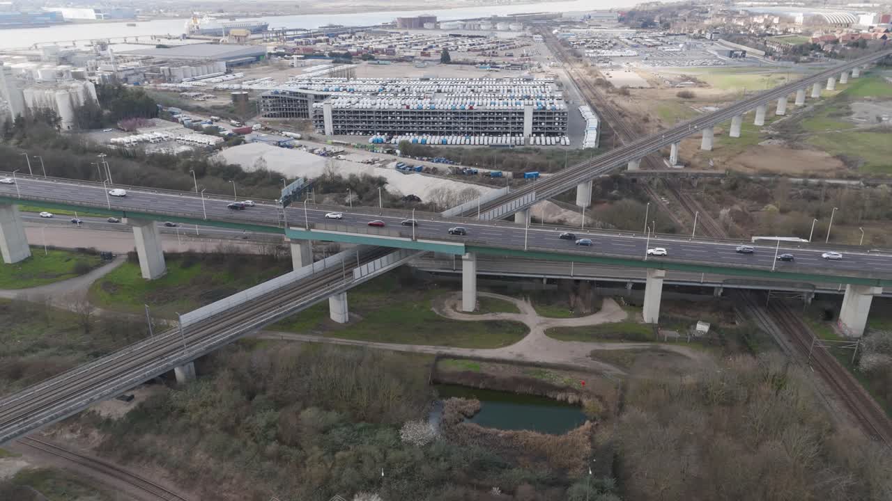 Aerial tracking shot sweeping multilayer flyovers packed with traffic on the A282 trunk road, curved ramps and bridges threading through industrial outskirts
